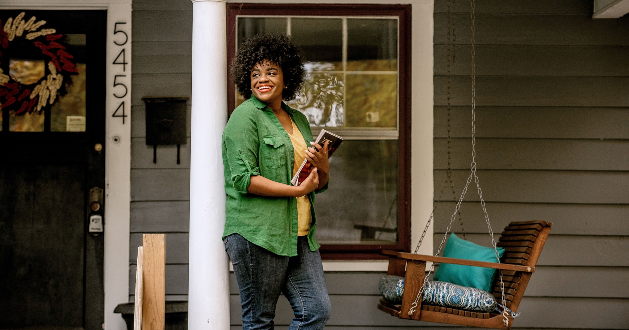 Black woman outside her front door leaning against pillar
